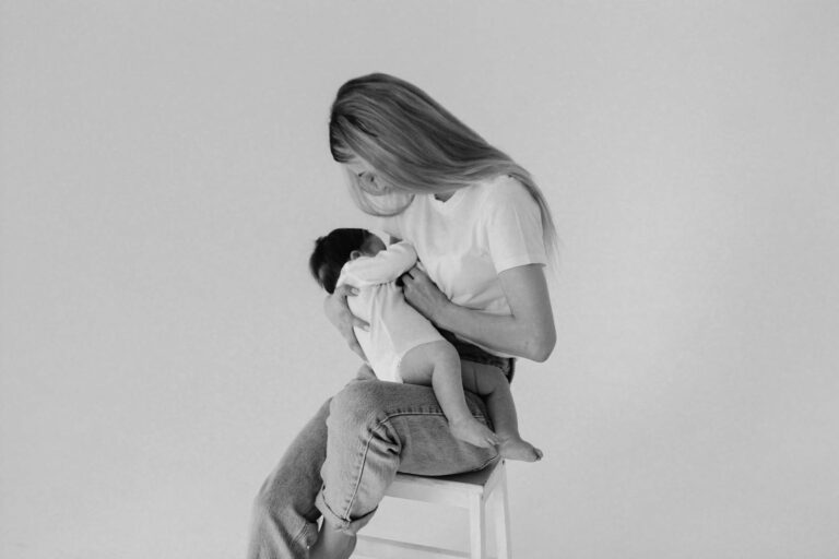 A heartwarming monochrome photo of a mother breastfeeding her baby while sitting on a stool in a studio.