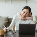 A mother works from home with her daughter embracing her, showing love and family connection.